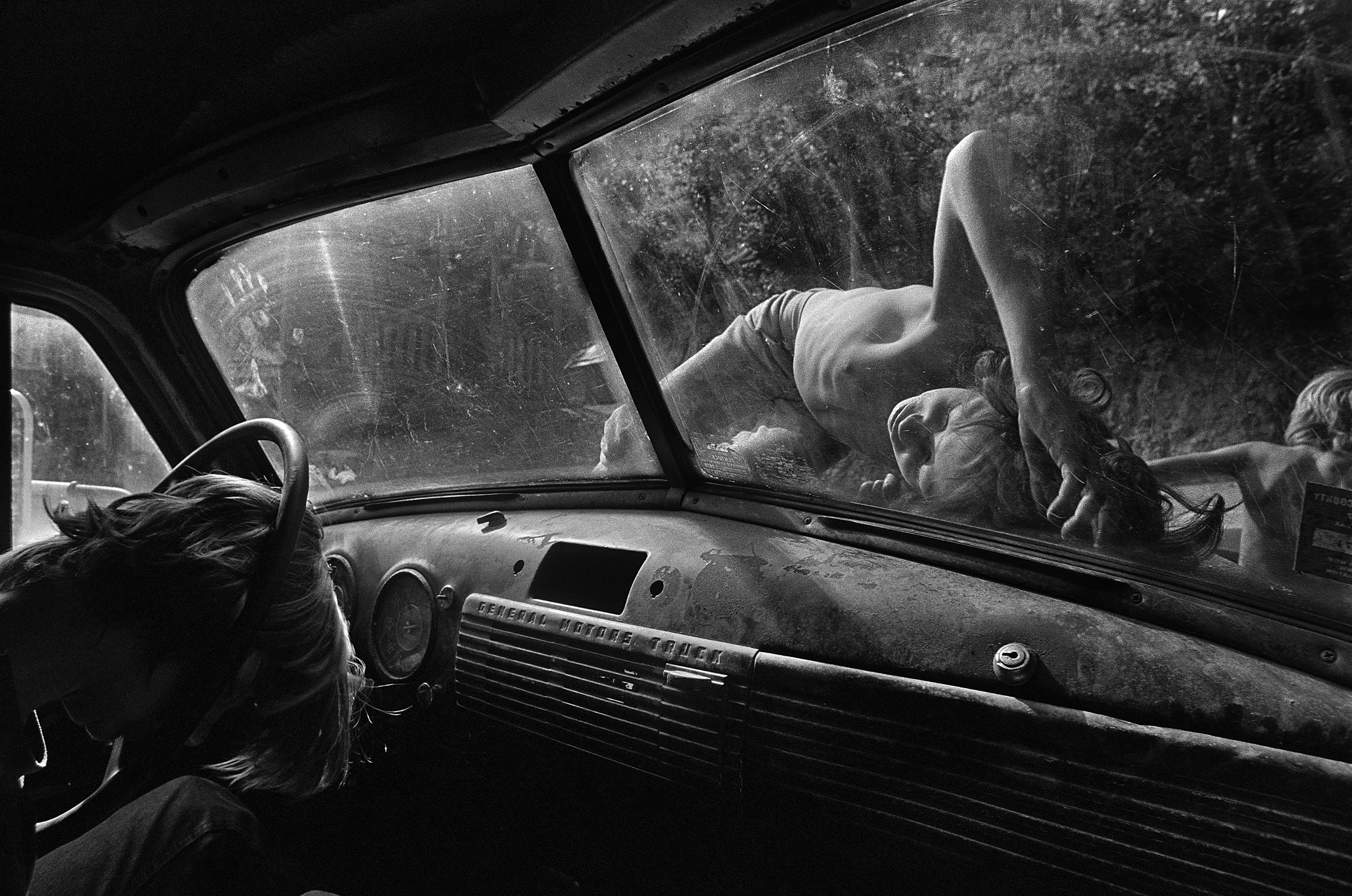 Caption: Boys sleep on the hood of a pickup truck on a hot summer day in Still House Hollow, Tennessee.Title: Still House Hollow, Tennessee, 1986